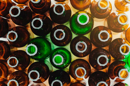 Seen from above, many empty green and brown glass bottles standing upright. In one corner a glow of light enters.の写真素材