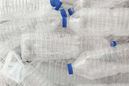 A pile of empty transparent plastic water bottles with blue caps seen from above.
