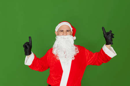 An adult Caucasian man dressed as Santa Claus is dancing with his index fingers up. The background is green.の写真素材
