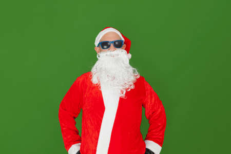 A Caucasian man dressed as Santa Claus wearing sunglasses looking straight ahead. The background is green.の写真素材