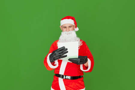 A Caucasian man dressed as Santa Claus is reading a letter while holding it together with a light green envelope. The background is green.の写真素材