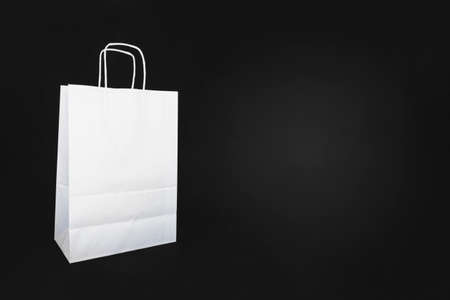 On a black background there is, isolated, a white colored paper shopping bag. On one side there is a lot of copy space.の写真素材