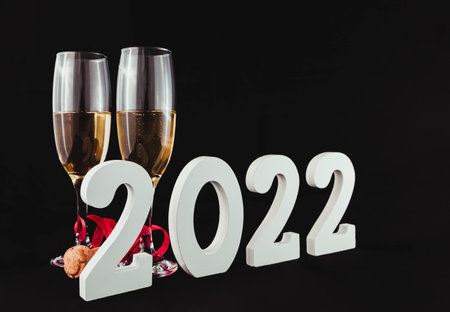 On a black background there are two crystal glasses with champagne, a red ribbon and a cork stopper....