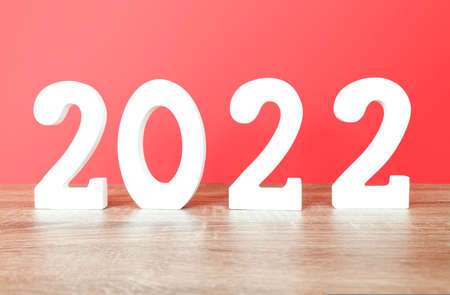 The number 2022 made with white colored wooden numbers planted on an oak colored wooden surface and red background.の写真素材