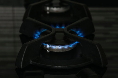 The hob of a gas stove in a kitchen lit with a blue flame. The surface is made of glass and the support is metal.の写真素材