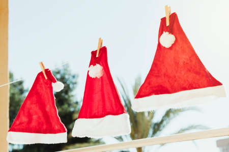 Three Santa Claus hats hanging from a clothesline, one of them is in focus, the rest are blurred. In the background you can see the sky and trees.の写真素材