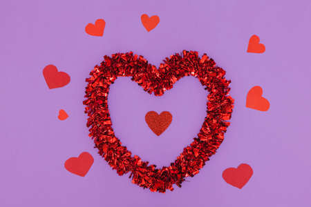 On a violet background there are several hearts, one of them is larger and brighter and the rest are small. In the center of the large heart is a small red glitter heart.の写真素材