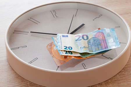 There are two 20 euro bills and one 50 euro bill on a large round clock. The clock strikes ten to two.の写真素材