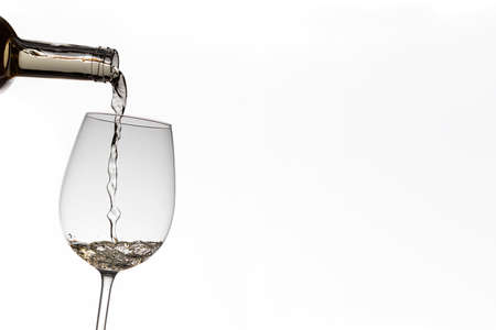 A bottle filling a tilted white wine glass. The liquid is in motion which remains frozen. On one side there is a lot of copy space. The background is white.の写真素材