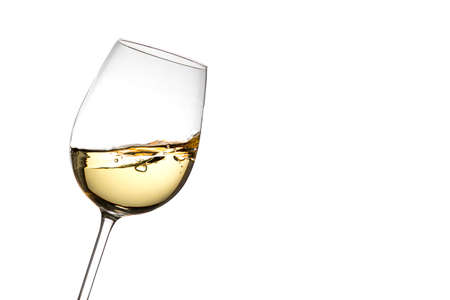 On a white background, isolated, a tilted crystal glass filled with moving white wine which is observed frozen. On one side there is a lot of copy space.の写真素材
