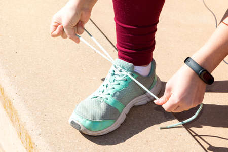 Close-up of a girl dressed in maroon leggings and turquoise sneakers is tying her shoelaces.の写真素材