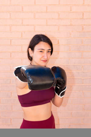 A young Caucasian woman wearing black boxing gloves is punching in front. The punching fist is in focus and the rest is out of focus. In the background is a brick wall.の写真素材