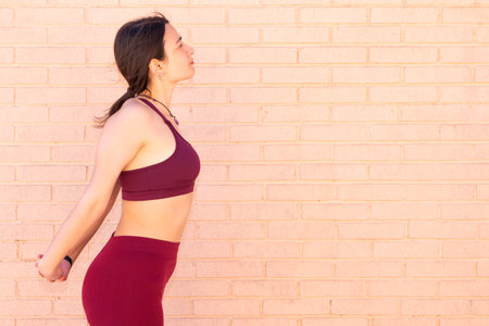A young Caucasian woman dressed in a top and leggings is doing arm, chest and back stretches next to...
