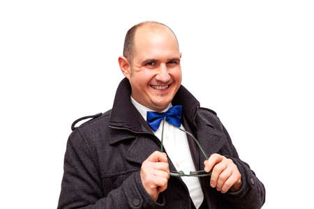 A bald Caucasian adult male well dressed in a suit, shirt, bow tie and jacket is holding a pair of sunglasses with his hands. The background is white.の写真素材