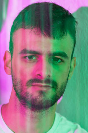 Portrait of a young Caucasian man with a beard behind a glass in which reflections can be seen. It...
