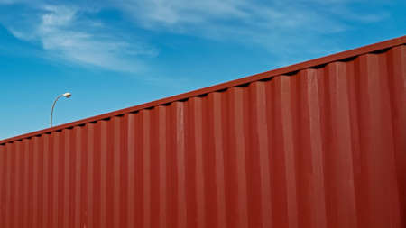 Part of a red cargo container with blue sky with some clouds and a streetlight on background.の写真素材