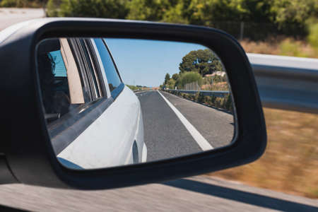 Rearview mirror of a white car driving on a highway, which is reflected in the mirror. In the background you can see the sweeping movement of the exterior.の写真素材