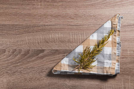 Cloth napkin with white, gray and brown checkered pattern, on which there is a branch of rosemary. It is isolated on a wooden table.の写真素材