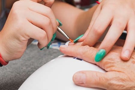 Close-up of the hands of two unrecognizable women, one young and one old, having a manicure. The...