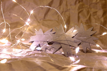 Three cardboard snowflakes handmade from a toilet paper tube on a crumpled paper surface with Christmas lights around them.の写真素材