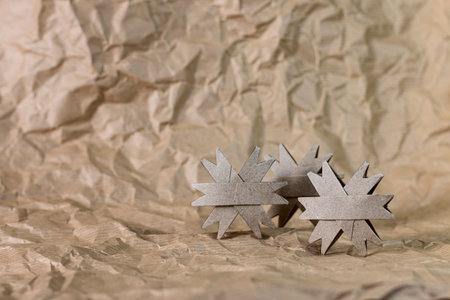 Three handmade cardboard Christmas snowflakes made from a toilet paper tube isolated on a crumpled paper surface and background.の写真素材