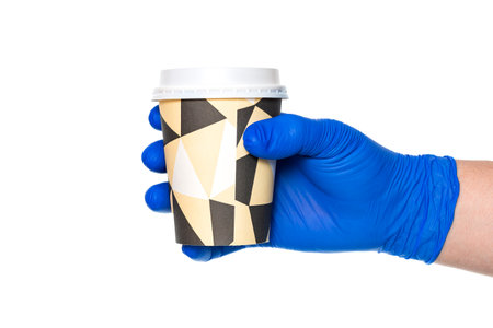 Crop anonymous hand of doctor in latex glove holding paper coffee cup to go against white backgroundの写真素材