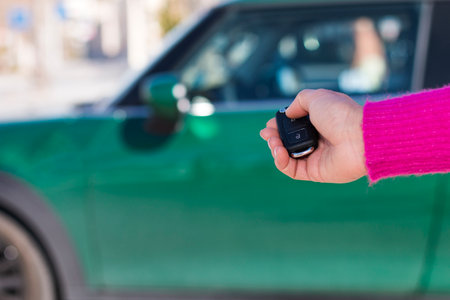 Crop female in pink sweater pressing button on remote car key while opening green vehicle against blurred backgroundの写真素材