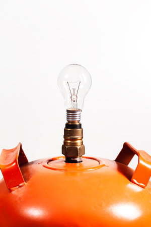 Close-up of an unlit light bulb placed in the valve of an orange domestic gas tank over white background.の写真素材