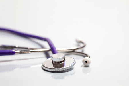 Close-up of a stethoscope's bell over a white surface where it is reflected. The tubing is purple and earpieces are white.の写真素材