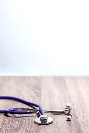 Close-up of the bell and earpiece of a stethoscope on a wooden table. A white wall is on background.の写真素材