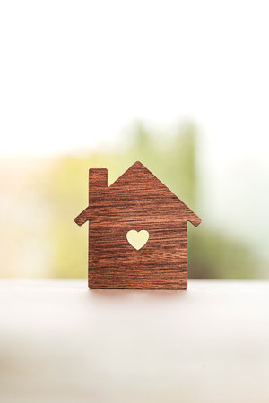 Close up shot of a silhouette in the shape of a house with a heart-shaped hole in the center on a table with a window in the background.の写真素材
