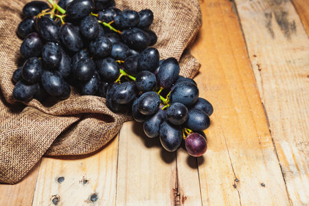 Close-up of a bunch of dark grapes on a rustic wooden table and a sackcloth.の写真素材