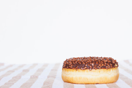 Delicious sweet donut covered with glaze and sprinkled with chocolate chip served on striped napkin...
