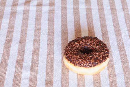 High angle of appetizing donut covered with chocolate glaze and sprinkles served on white and brown striped tableclothの写真素材