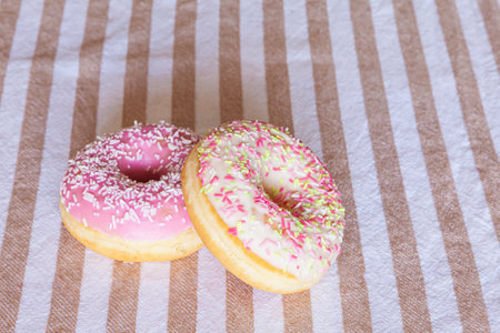 High angle of delicious donuts with pink and white glaze sprinkles and strawberry flavor served on striped tableclothの写真素材