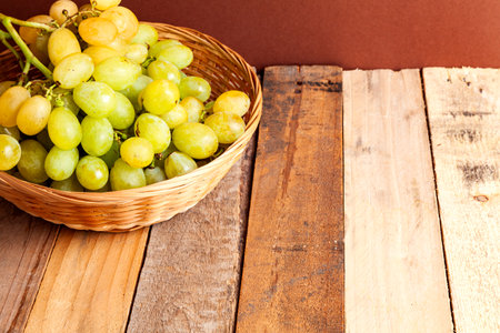 From above of fresh ripe organic grape fruits with stem in wicker basket while placed on wooden table in room with brown wall in daylightの写真素材