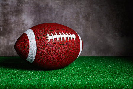 An American football ball over a ground with green grass in front of a concrete wall.の写真素材