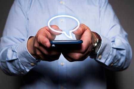 Close-up of unrecognizable caucasian man's hands holding a mobile phone while he can see a virtual comic bubble icon floating over the smartphone.の写真素材