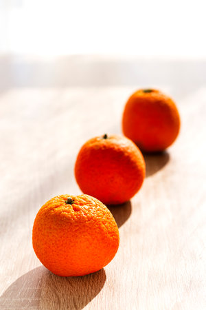 Three tangerines lined up on a wooden table in front of a window, the first one is in focus, the rest are out of focus.の写真素材