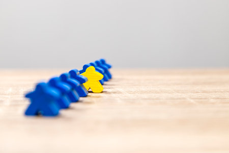 A yellow game piece positioned ahead of a row of blue pieces on a wooden background, symbolizing leadership.の写真素材