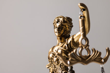 Close-up shot of the head of a golden statue of the goddess of justice with blindfolded eyes holding a scale against a gray backgroundの写真素材