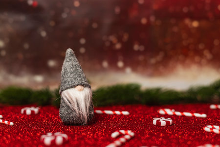 Gray plush Santa is sitting on a red glitter surface. There are candy canes in the background.の写真素材