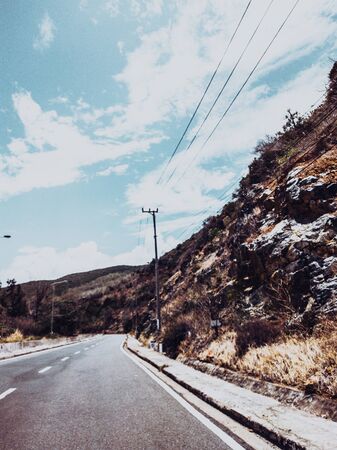 Dry asphalt empty automobile road with marking lines near rocks on a sunny summer day with blue cloudy sky. Car travel trip concept background. Stories vertical format. Dark green style.の写真素材