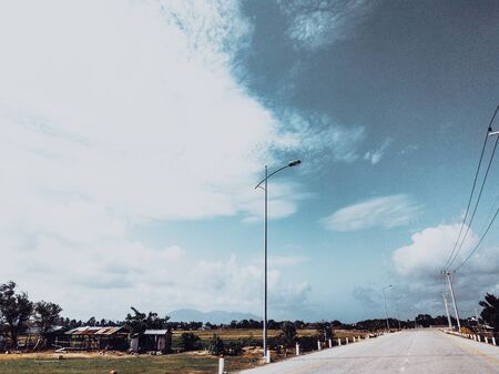 Beautiful view of dry asphalt empty automobile road with marking lines near meadow on a sunny summer day with blue cloudy sky. Car travel trip concept background. Dark green style.の写真素材