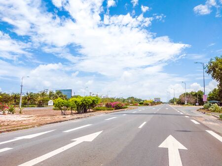 Beautiful view of wide open road with a paved highway stretching out as far as the eye can see with small green hills, pink flowers under a bright blue sky in the summer time.の写真素材