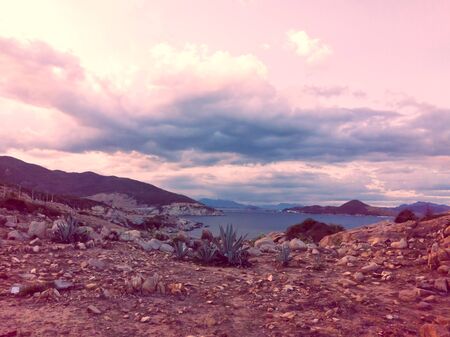 Beautiful dramatic dark blue pink sunset sky with clouds over the sea and rock stone mountainsの写真素材