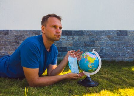 Man wearing Face Mask holding the Earth globe world map in hand. Quarantine yourself to protect spread virus. When can travel again. Epidemic pandemic coronavirus 2019-ncov sars covid-19 virus conceptの写真素材