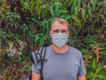 Portrait of guy with a medical mask. Outside walking in the Mango trees garden. He wants to breathe, wait for the end of quarantine Covid19 isolation and beginning of normal life againの写真素材