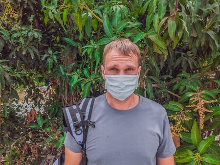 Portrait of guy with a medical mask. Outside walking in the Mango trees garden. He wants to breathe, wait for the end of quarantine Covid19 isolation and beginning of normal life againの写真素材