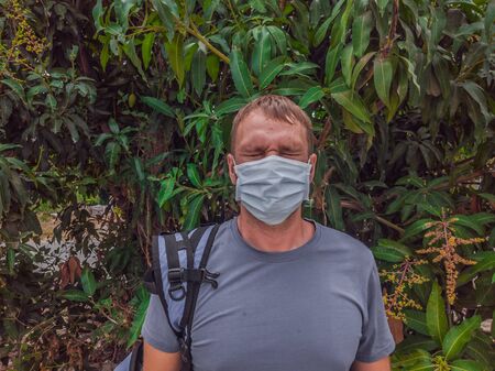Portrait of guy with a medical mask. Outside walking in the Mango trees garden. He wants to breathe, wait for the end of quarantine Covid19 isolation and beginning of normal life againの写真素材